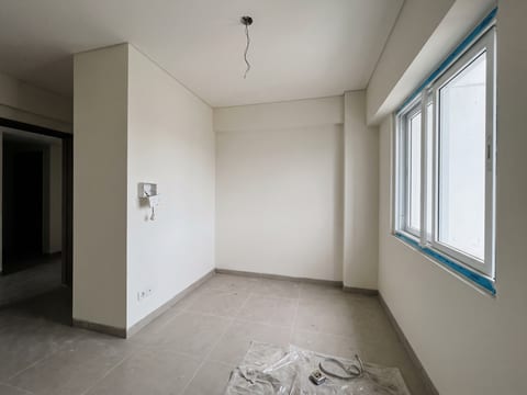 Sebelum — kamar kedua kosong tanpa penyimpanan, stop kontak menonjol di dinding, plastik pelindung masih menempel