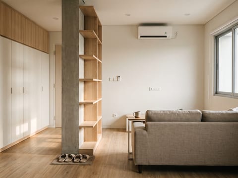 Ruang tamu apartemen dengan lemari HPL oak natural setinggi plafon dan kolom struktur dibungkus rak dua sisi