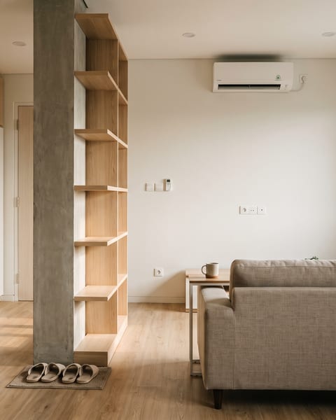 Ruang tamu apartemen dengan lemari HPL oak natural setinggi plafon dan kolom struktur dibungkus rak dua sisi