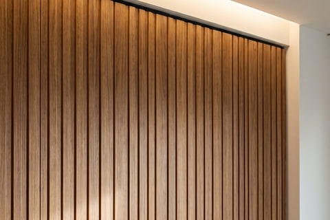 Detail wall panel HPL kayu dengan alur vertikal, pertemuan panel dengan plafon gypsum dan cove lighting
