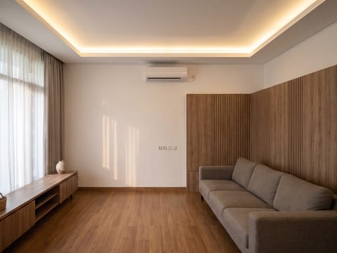 Ruang keluarga dengan wall panel HPL kayu beralur vertikal dan plafon gypsum datar dengan cove lighting