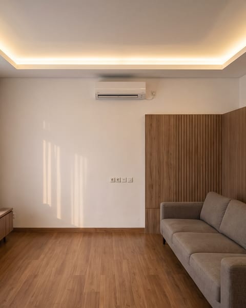 Ruang keluarga dengan wall panel HPL kayu beralur vertikal dan plafon gypsum datar dengan cove lighting