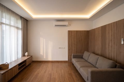 Ruang keluarga dengan wall panel HPL kayu beralur vertikal dan plafon gypsum datar dengan cove lighting