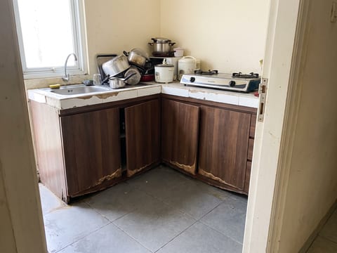 Sebelum — dapur bawaan dengan pintu kabinet bawah yang melengkung dan peralatan menumpuk di meja