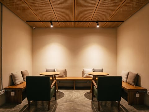Zona duduk lounge di bagian belakang ruko dengan dinding terang, track light, dan panel akustik kayu berlubang