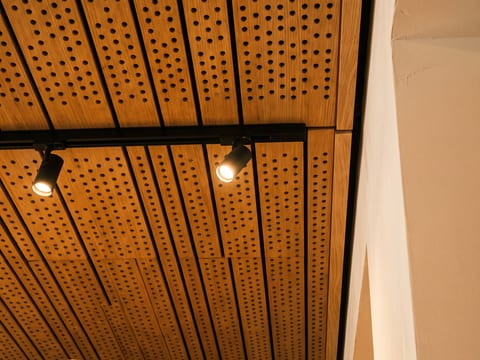 Panel akustik kayu berlubang pada plafon di belakang bar kedai kopi