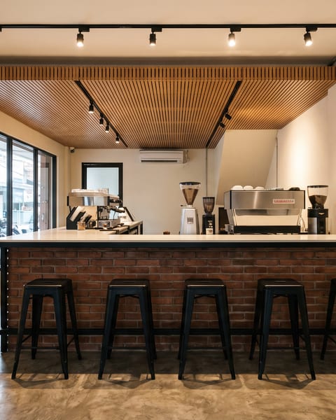 Bar kedai kopi di tengah bentang ruko dengan rangka besi hollow, top solid surface, dan panel bata ekspos