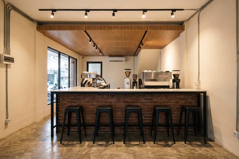 Bar kedai kopi di tengah bentang ruko dengan rangka besi hollow, top solid surface, dan panel bata ekspos