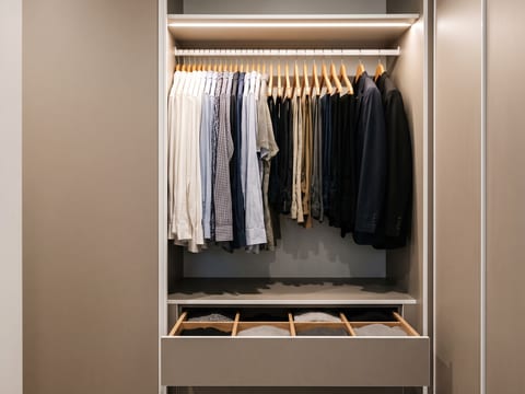 Sisi kiri lorong closet berisi gantungan panjang untuk pakaian kerja dan laci dengan rel soft-close