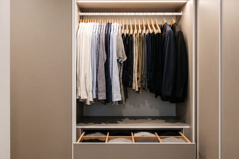 Sisi kiri lorong closet berisi gantungan panjang untuk pakaian kerja dan laci dengan rel soft-close