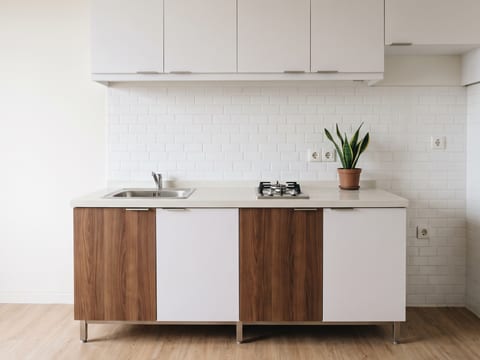 Dapur kompak unit studio dengan kabinet HPL putih, top solid surface, dan kaki stainless 10 cm