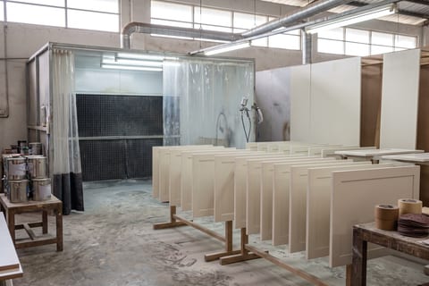 Area finishing workshop dengan panel pintu kabinet disusun untuk pengeringan setelah pengecatan